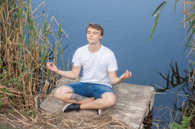Genç bir adam gölün kıyısında meditasyon yapıyor.