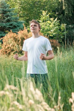 güçlü kırsal Slav genç adam uzun otların üzerinde duruyor.