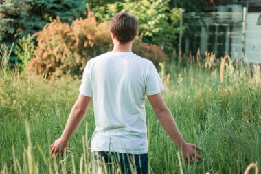 Genç adam uzun çimlerin üzerinde duruyor.