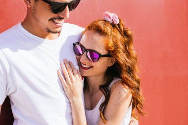 Genç çift kırmızı arka planda sarılıyor ve gülümsüyor.