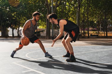 Dışarıda basketbol oynayan iki genç adam top için dövüşüyor.