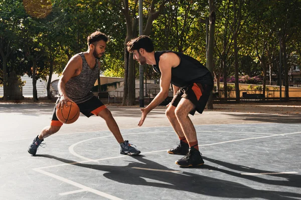 Dışarıda basketbol oynayan iki genç adam top için dövüşüyor.