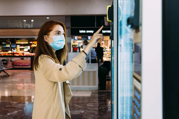 Yüz maskeli kadın yiyecek almak için otomatı kullanıyor.