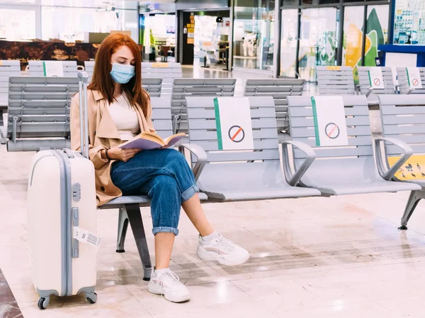 Yüz maskeli kadın tren istasyonunda otururken kitap okuyor.