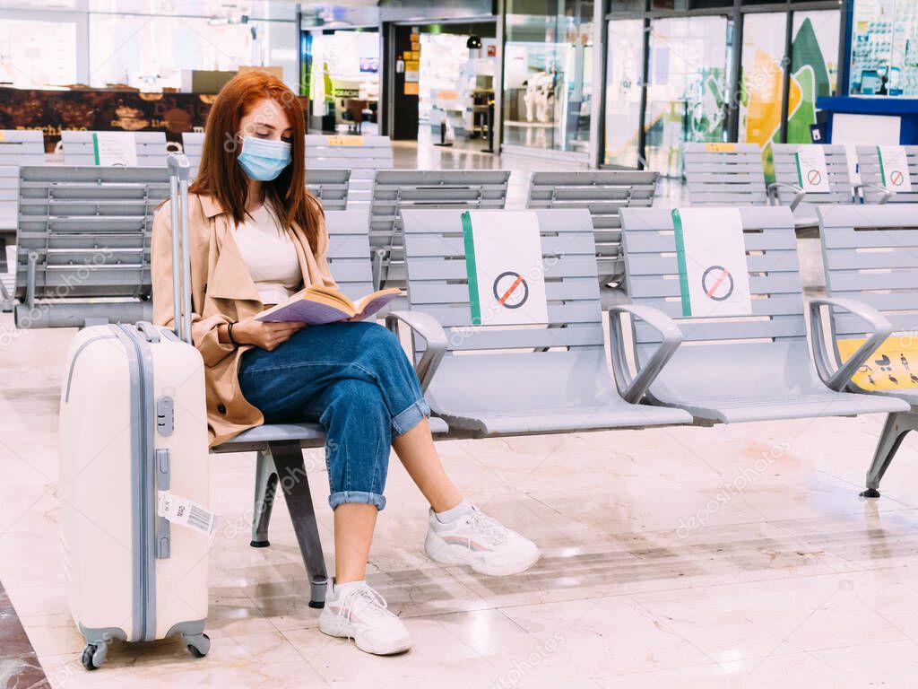 woman with a face mask reads a book while sitting at the train station