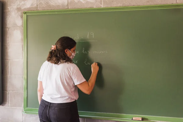 teacher writes on the board the measures to protect herself from the coronavius