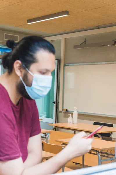 teacher with a face mask checks his schedule on his smartphone in an empty classroom