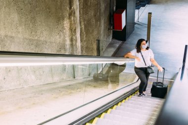 Metroda yürüyen merdivende koruyucu yüz maskesi takan genç bir kadın..