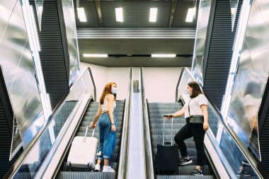 Yüz maskesi takan iki genç turist metro yürüyen merdivenlerini kullanıyor.