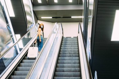 Yüz maskeli genç turist metro yürüyen merdiven kullanıyor.