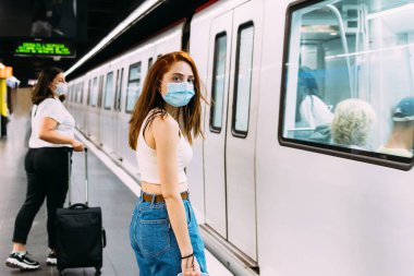 Yüzü maskeli genç bir kadın metroyu bekliyor.