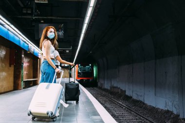 Yüzü maskeli genç bir kadın metroyu bekliyor.
