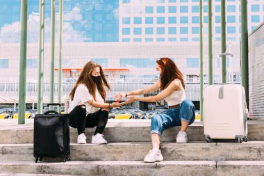 Yüz maskesi takan iki genç turist güvenli bir mesafede oturuyorlar çünkü covid-19 ellerini temizlemek için anti-bakteri jeli kullanıyorlar.