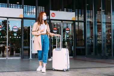 Yüzü maskeli bir turist, tren istasyonundan bavulunu taşıyarak ayrılıyor.