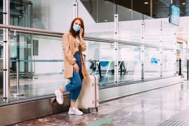 Tren istasyonunda akıllı telefonunu kullanan maskeli bir kadın.