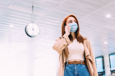 Tren istasyonunda akıllı telefonunu kullanan maskeli bir kadın.