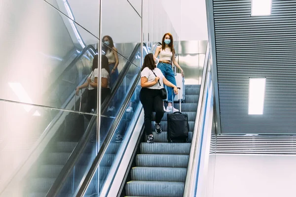 Yüz maskesi takan iki genç turist metro yürüyen merdivenlerini kullanıyor.