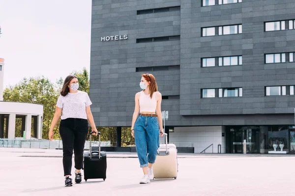 Maskeli iki genç turist Covid-19 nedeniyle güvenli bir mesafede kalarak otelden ayrılıyor.