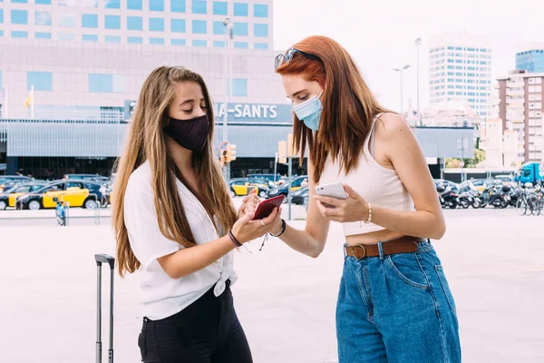 Yüz maskeli iki genç turist akıllı telefonlarıyla otelin adresini arıyorlar.