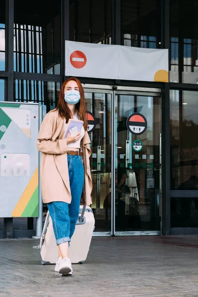 Yüzü maskeli bir turist, tren istasyonundan bavulunu taşıyarak ayrılıyor.