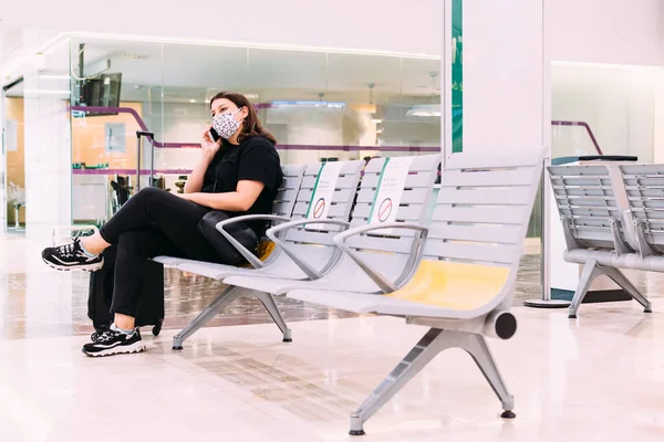 Yüz maskeli kadın tren istasyonunda otururken akıllı telefonunu kullanıyor.