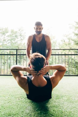 Yüz maskesi takan antrenör, genç adamın mekik çekmesine yardımcı oluyor.