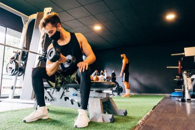Koruyucu yüz maskesi takan genç adam spor salonunda çalışıyor.