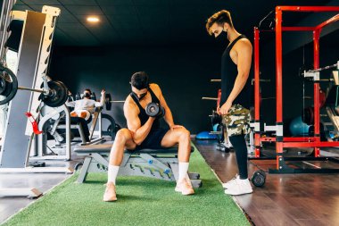 Koruyucu yüz maskesi takan genç adam spor salonunda çalışıyor.