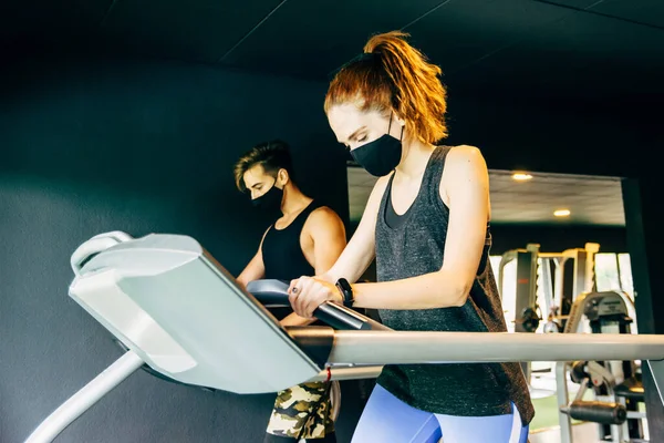 Genç bir kadın ve maske takan genç bir adam spor salonunda çalışıyor.