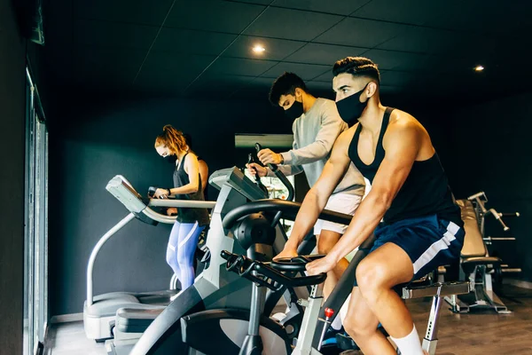 Spor salonunda çalışan yüz maskesi takan bir grup genç.