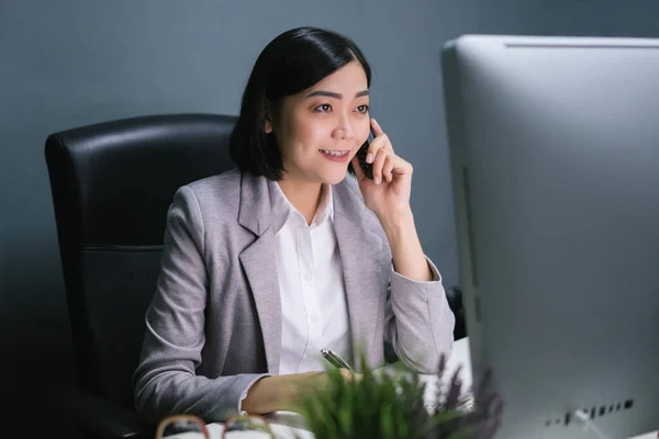 Happy asian business woman at her office desk answering phone and smiling.Happy business woman.