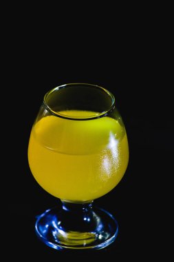 Siyah arka planda portakal suyu olan bir bardak.