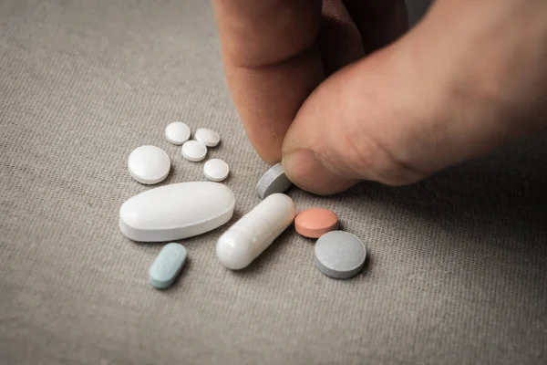 Bir erkek eli bir avuç hapa uzanıyor ve mavi bir hap alıyor. Fotoğraf, yumuşak ışık ve minimalist gri arkaplanlı..