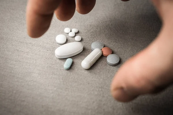 Bir erkek eli bir avuç hapa uzanıyor. Fotoğraf yumuşak ışıklandırma ve minimalist gri arkaplan ile çekilmiştir..