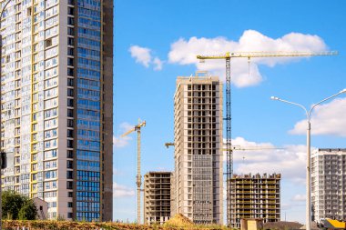 Modern bir bina inşaatı. Bir sürü yüksek katlı vinç. Mavi gökyüzünün arka planında sarı inşaat vinci