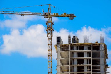 Mavi gökyüzüne karşı sarı bir inşaat vinci olan yüksek binalı bir bina.