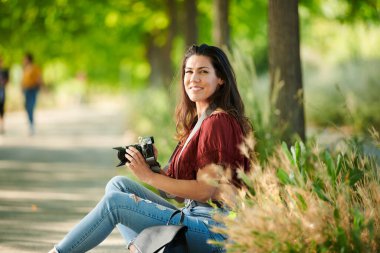 Rahat öğrenci elinde kamerayla parkta oturdu.