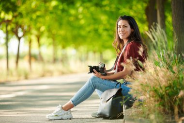 Rahat öğrenci elinde kamerayla parkta oturdu.