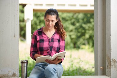 Üniversite kampüsünün köşesinde oturan bir öğrenci kitap okuyor.