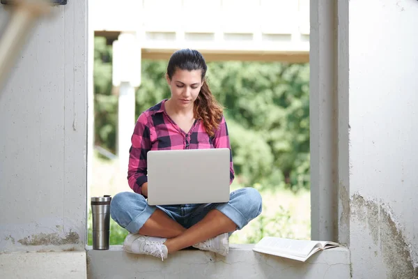 a student writes on a laptop sitting in a corner of the university campus