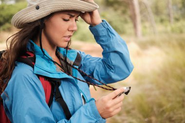 Yürüyüş için giyinmiş kırmızı sırt çantalı esmer kız bir pusula endişeli görünüyor.