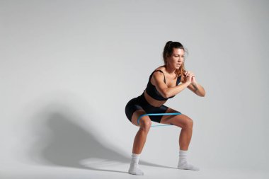 Siyah giyinmiş fitness kızı bacaklarıyla prezervatif takıyor ve çömeliyor.
