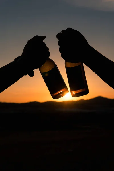 A silhouette of two young men toasting for they friendship from a beautiful sunset