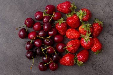 Masada bir avuç kiraz ve çilek. Koyu taş desenli.
