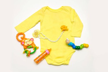 Bebek sarısı tulumu, çıngırak, emzik, oyuncak. Beyaz arka planda çocuk kıyafetleri ve aksesuarlar