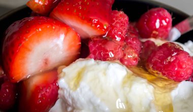 A yakın çekim bir kase çilek, ahududu ve üstte ballı yoğurt