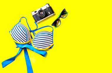 Düz Lay Bikini, vintage fotoğraf makinesi, güneş gözlüğü ve kabuk üzerinde sarı renkli şık modern moda arka plan ile. Tatil seyahat yaz hafta sonu deniz macera seyahat kavramı