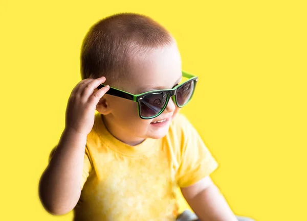 Happy smiling boy in yellow t-shirt and green sunglasses, childhood, fashion and people concept, on yellow background, summer time