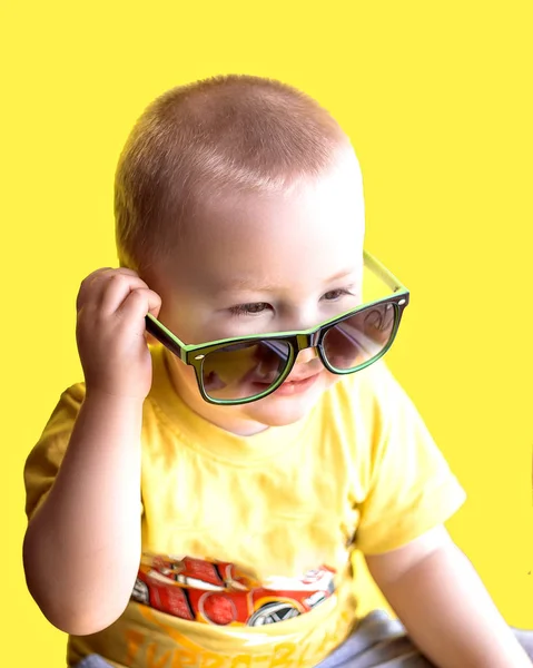 Happy smiling boy in yellow t-shirt and green sunglasses, childhood, fashion and people concept, on yellow background, summer time