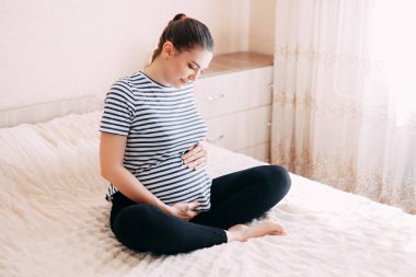 Hamilelik, dinlenme, insanlar ve beklenti konsepti mutlu hamile bir kadın yatakta oturup karnına dokunuyor.